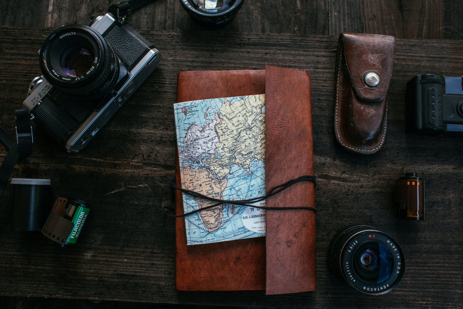 Top view of notebook with map for traveling placed on wooden surface near retro photo camera with film and lens near knife case