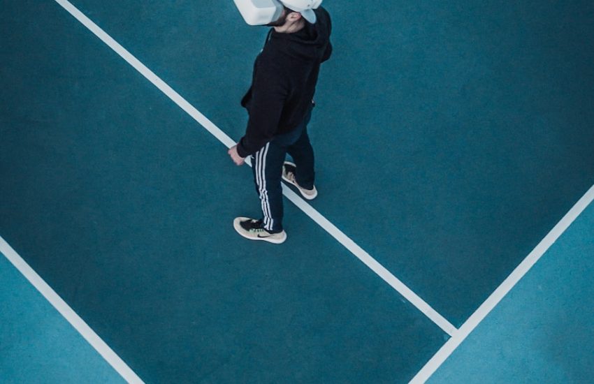 man in track suit wearing VR headset standing on tennis court